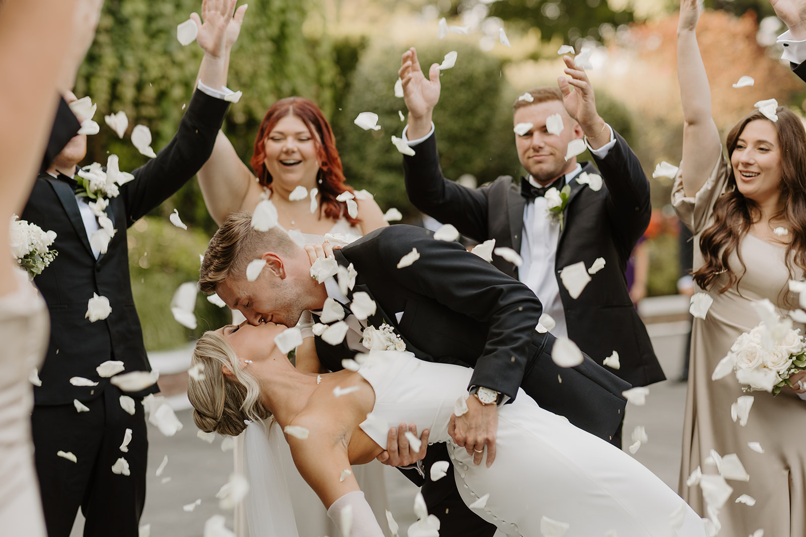 Close-up of the groom dipping and kissing the bride as white rose petals rain down during their celebration.